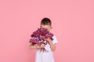 Little boy with bouquet of lilac flowers on pink background