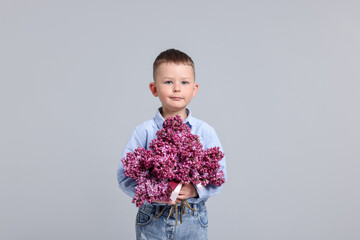 Little boy with bouquet of lilac flowers on light grey background