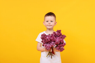 Little boy with bouquet of lilac flowers on yellow background
