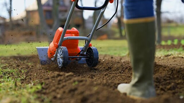 Woman preparing garden beds for planting. Rotovator, garden tiller, rotary tiller or mini cultivator. Cultivators break up compacted soil, improve its structure and aeration.