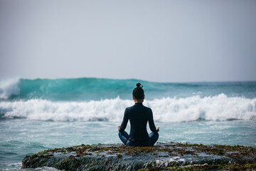Yoga woman meditation at the seaside cliff edge facing the coming strong sea waves