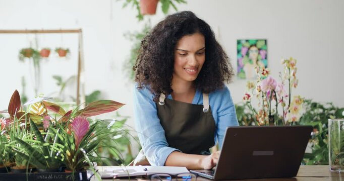 Young African American woman flower business owner in apron using laptop working at the floral store they checking the inventory. Floristry and modern technology concept.