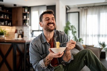 Happy man eating instant noodles at home, enjoying a quick meal