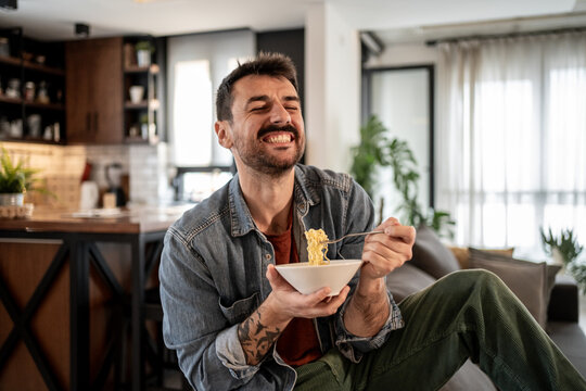 Happy man eating instant noodles at home, enjoying a quick meal