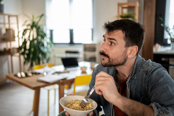 Freelancer eating noodles and looking away while working from home