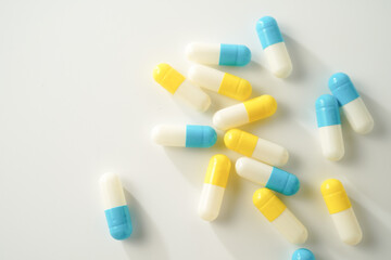 Capsules pill white blue yellow scattered on white surface, health care, medical background