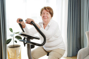 Senior woman training at home on a bicycle trainer, healthy lifestyle after retirement