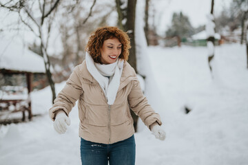 Obraz premium A cheerful woman in a warm jacket enjoys outdoor fun in a snowy landscape. Her joyful expression conveys happiness while embracing the beauty of a crisp winter day surrounded by white snow.