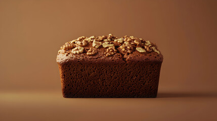 A loaf of brown cake topped with nuts against a brown background.
