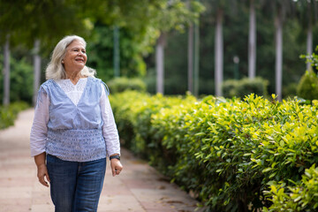 Fototapeta premium Portrait of smiling senior woman walking relaxed outdoors. Enjoying the little things. fun and spends time in nature, summer lifestyle during sunny day, happy retirement