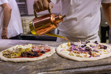 Pizzaiolo mentre condisce due pizze napoletane tradizionali con l'olio d'oliva prima di infornarle