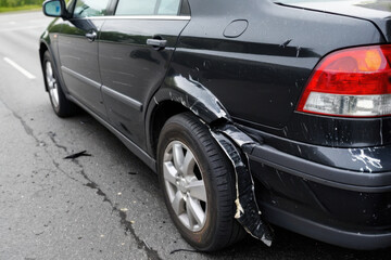 A black car with a dent on its side, photographed from an angle