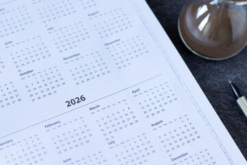 2026 calendar year in notebook planner with dates, weeks, and months and hourglass on a desk....