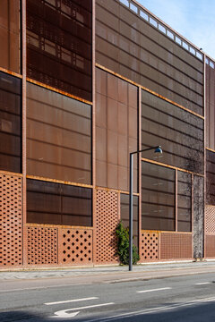 Textured facade of brown brick and metal panels with a single tree, offering contrast and symmetry for stock use in architecture and urban development themes.