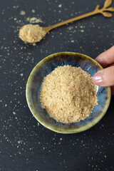 Hand is holding a bowl with nutritional yeast flakes. Top view. Healthy vegan cheese substitute.