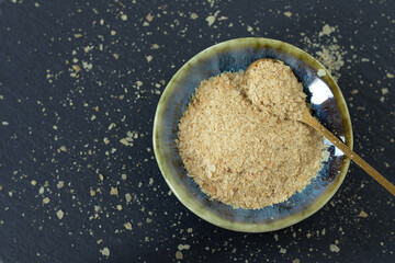 Nutritional yeast flakes in bowl with spoon on dark background. Top view. Vegan cheese substitute food.