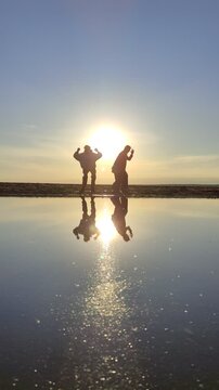 Happy family at sunset on the sea.
Silhouettes of people dancing on the shore and reflected in the water.