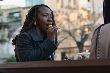 Woman sharing and enjoying a fruit salad with her friend outdoors.