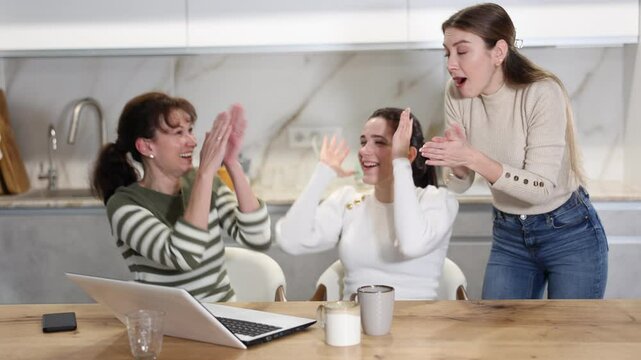 Joyful middle-aged women gloating over having won a prize sitting at notebook in the kitchen