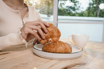 A woman enjoys a peaceful morning breakfast, holding a warm cup of coffee and a slice of bread in soft sunlight, embracing simplicity.
