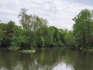 Small island emerging from dark water surrounded by lush trees under cloudy sky Reservoir Hostivar in Prague