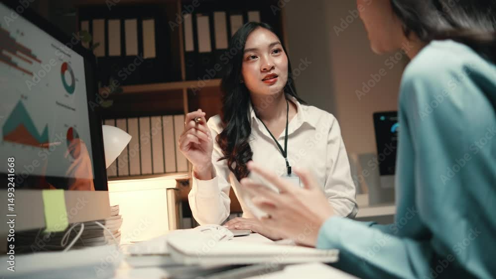 Poster two businesswomen discuss and analyze data displayed on a computer screen in a modern office setting