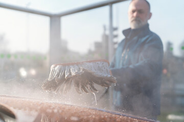 Close-up of Car wash process in a bright and sunny location with foam and driver using a brush to clean vehicle exterior