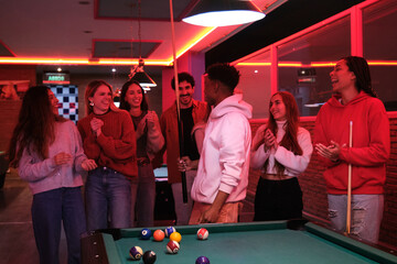 Group of friends having fun playing pool in a nightclub, clapping hands
