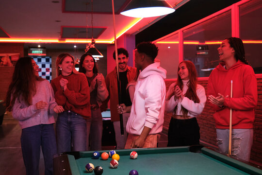 Group of friends having fun playing pool in a nightclub, clapping hands