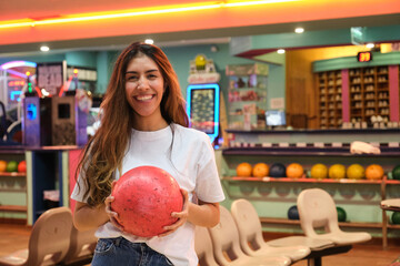 Fototapeta premium Happy woman holding a red bowling ball, smiling in a bowling alley