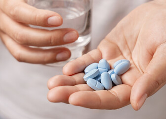 Woman in white t-shirt holding blue pills in cupped hand and water glass in hand closeup