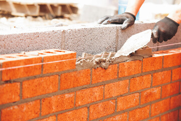 Skilled bricklayer laying bricks with trowel on construction site