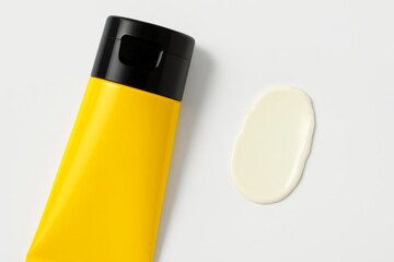 Glossy yellow cosmetic tube with a light cream smear on white background, vibrant and clean skincare layout