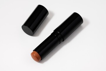 A sleek black cosmetic stick with a brown-toned product exposed, laying beside its detached cap on a bright white background