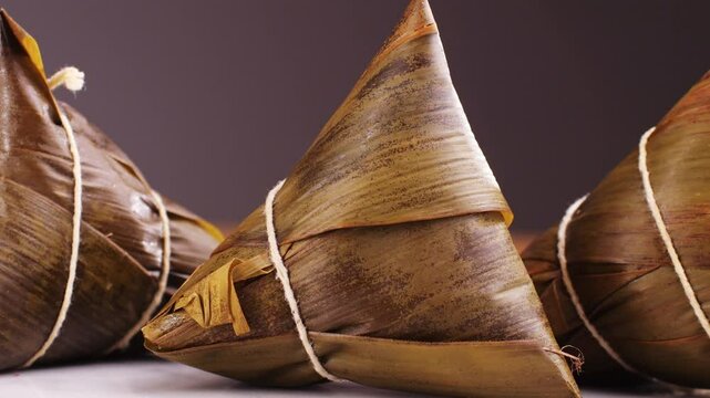 Hand holding zongzi (rice dumpling) with savoury fillings wrapped in bamboo or reed leaves.