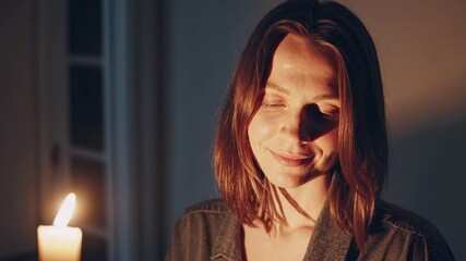 Woman enjoys a tranquil moment by candlelight, eyes closed in peaceful reflection. Soft shadows create a calming ambiance in her home