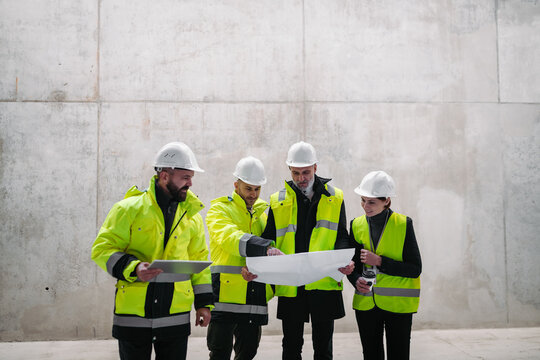 Team of engineers and construction workers reviewing blueprints, building site. - Powered by Adobe