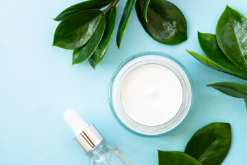 Natural cosmetic, cream jar with green leaves on blue.
