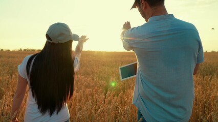 Two farmers shake hands with computer tablet, conclude contract in wheat field, sun. Work in team of business partners. Handshake of man of woman on field. Harvest, sale of grain Agricultural industry