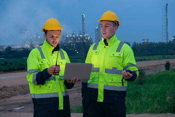 Two workers review project data at dusk in a construction site with industrial background