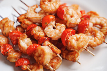 Skewers with shrimps and tomatoes on a white plate. 