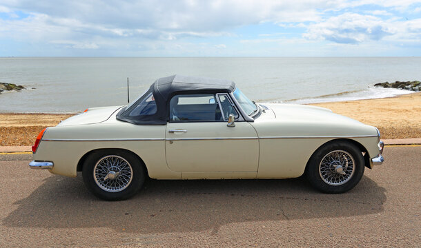 Classic White MGB Roadster parked on seafront promenade beach and sea in background