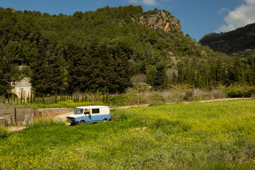 Fototapeta premium Old car abandoned in a field with yellow flowers surrounded by mountains on a sunny day