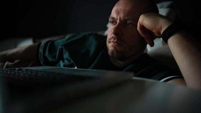 Middle-Aged Man in Teal Shirt Relaxing on Couch with Laptop


