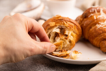 Croissant on white plate with hand on brown concrete background, cup of coffee, side view, close up, selective focus