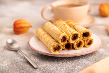 Waffles with caramel on brown concrete, orange textile, cup of coffee, side view, close up, selective focus
