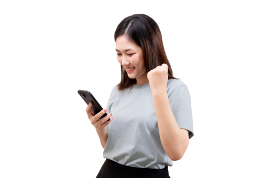 Asian young beautiful woman smiles while looking at her phone and raises her fist in a celebratory gesture.