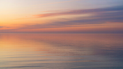 Obraz premium Beautiful serene sunset over calm ocean water with pastel color sky and reflections.