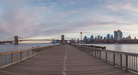 Wooden Pier Extending Towards Bridge and City Skyline Under Cloudy Sky