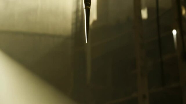 A golden spike or dart hangs suspended in a dark, misty industrial or fantasy environment illuminated by distant lights.
